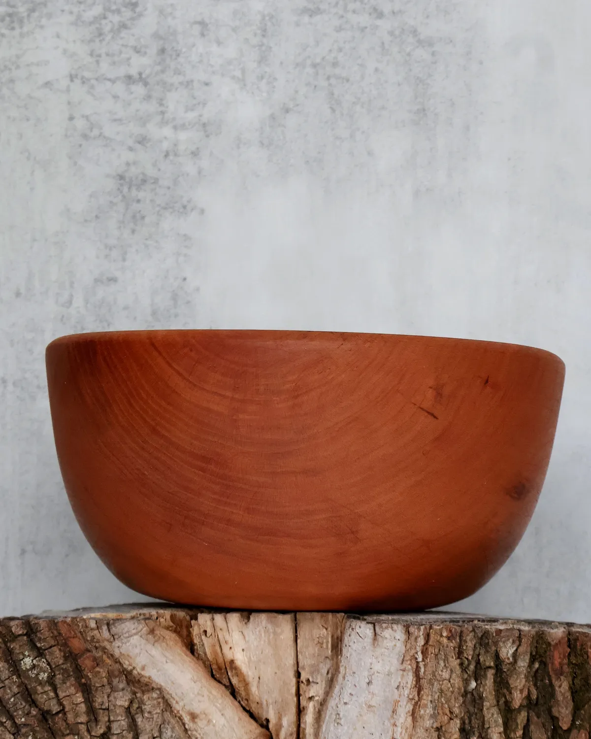 Hand-turned cherry wood bowl with smooth rounded profile on log stump