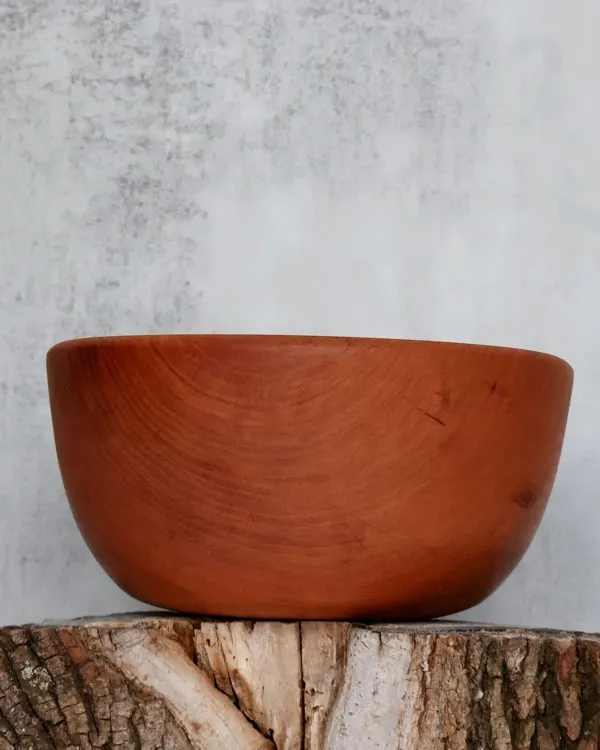 Hand-turned cherry wood bowl with smooth rounded profile on log stump